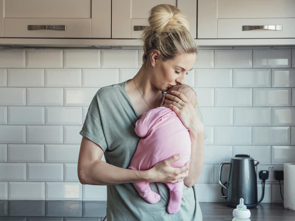 jovem mãe segura bebê contra o peito, com ternura, na cozinha